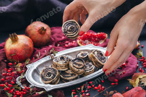 Preview: Female hands taking raw vegan puppy roll from a metal plate with rosehips and pomegranate seeds