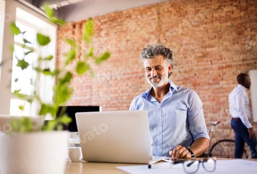 Preview: Smiling businessman using laptop in office with colleague in background
