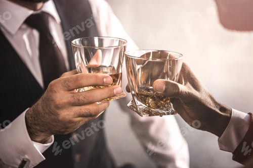 Preview: cropped shot of two men in formal wear clinking whiskey glasses