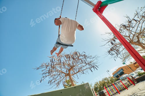 Preview: Man swinging on playground in sunlight