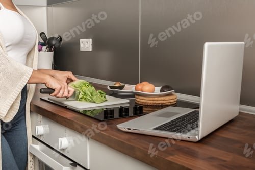 Preview: Crop woman cooking lunch and watching video on laptop