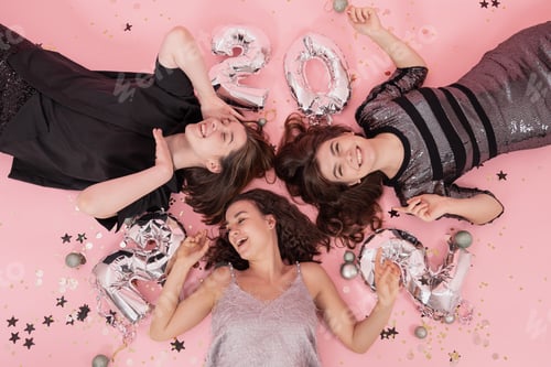 Preview: Cheerful girls lie on pink background with silver balloons 2022, top view.