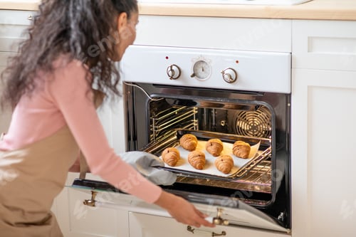 Preview: Unrecognizable Young Woman Taking Tray With Croissants Out Of Oven On Kitchen