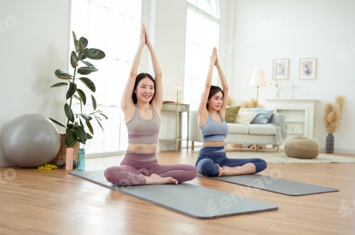 Preview: Two young Asian woman friends practicing yoga at home.