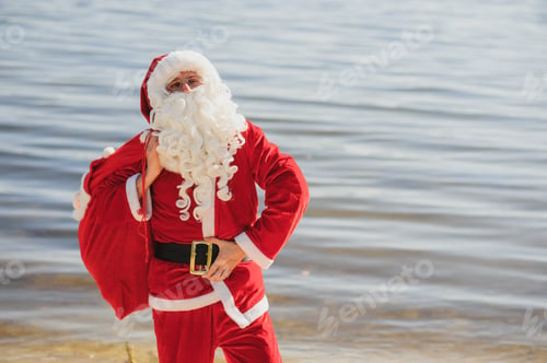 Preview: Santa Claus with at big Christmas sack full of gifts stay at ocean tropical sandy beach