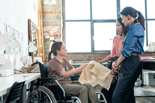 Preview: Young fashion designers talking to seamstress in wheelchair