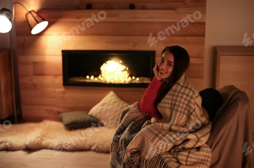Preview: Young woman resting near decorative fireplace at home. Winter season