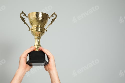 Preview: Man holding gold trophy cup on light grey background, closeup. Space for text