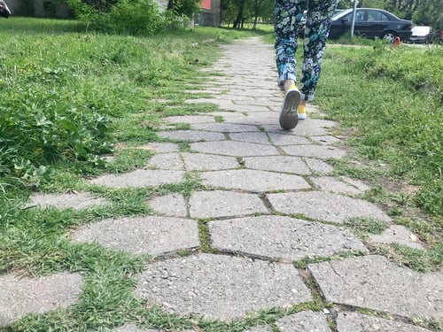 Preview: A woman with colorful pants and yellow shoes walking outside on a sunny day during Spring season.