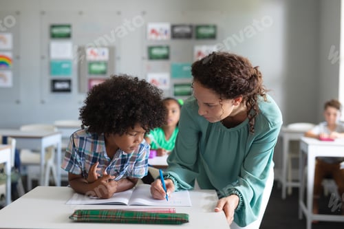Visualização: Professora caucasiana jovem auxiliando estudante do ensino fundamental afro-americano estudando na mesa