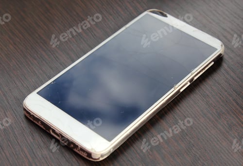 Preview: Dropped smartphone with broken screen on wooden table.