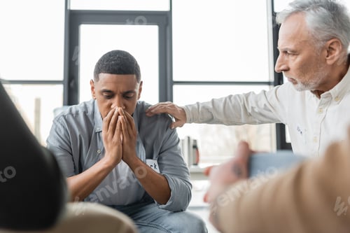 Preview: Middle aged man calming african american member of alcoholics meeting in rehab center