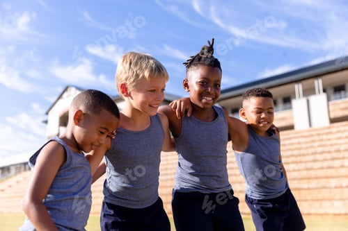 Preview: Smiling multiracial elementary boys standing with arm around against school building on sunny day