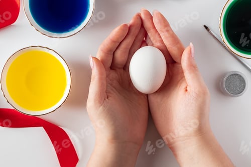 Preview: Woman hands holding white egg. Painting easter eggs for spring holiday.