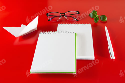Preview: Office supplies on a red background. Blank notebook, pen and glasses.
