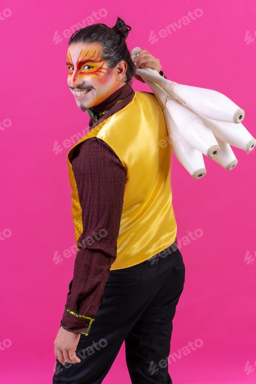 Preview: Funny circus performer holding clubs on his shoulder isolated on pink background