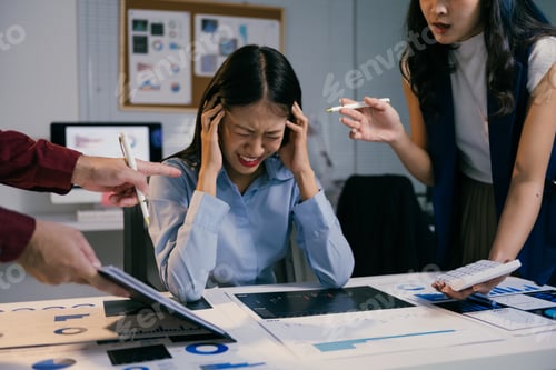 Preview: Young asian businesswoman suffering from headache while colleagues arguing and blaming her for bad w