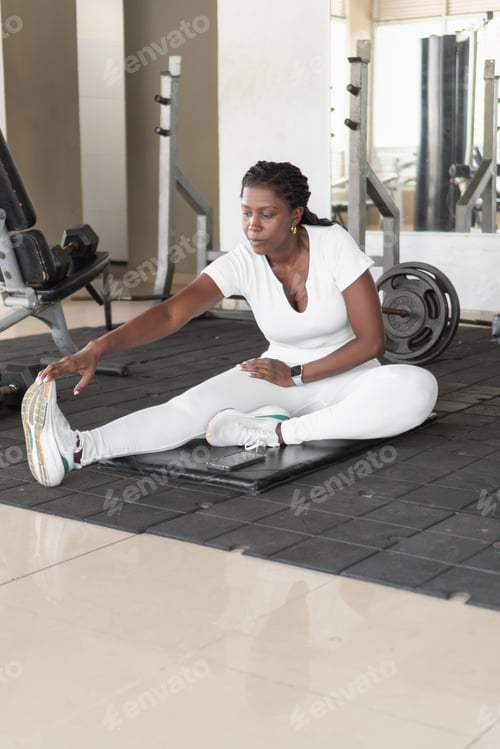 Preview: Mid adult woman stretching legs on gym floor after workout