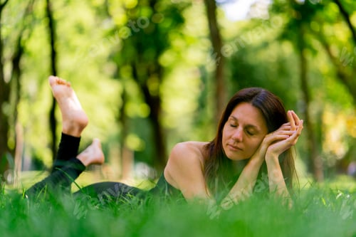 Preview: Active beautiful yogi woman resting in the city park after training lying on fitness mat