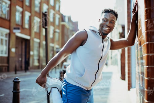 Preview: Athletic man stretching while leaning against a wall
