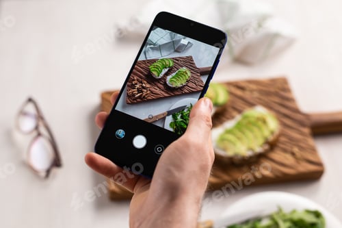 Preview: Hands take pictures on smartphone of two beautiful healthy sour cream and avocado sandwiches lying