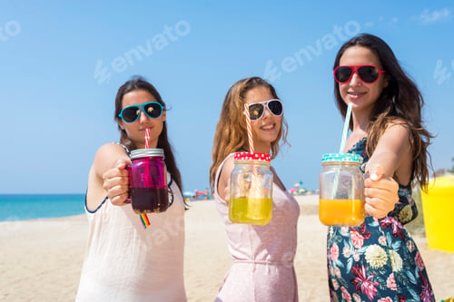 Preview: group of happy young women or female friends toasting non alcoholic drinks on summer beach