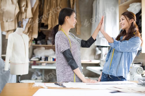 Preview: Two female fashion designers high fiving in studio
