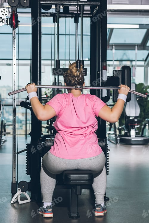 Preview: overweight woman working out on training apparatus at gym