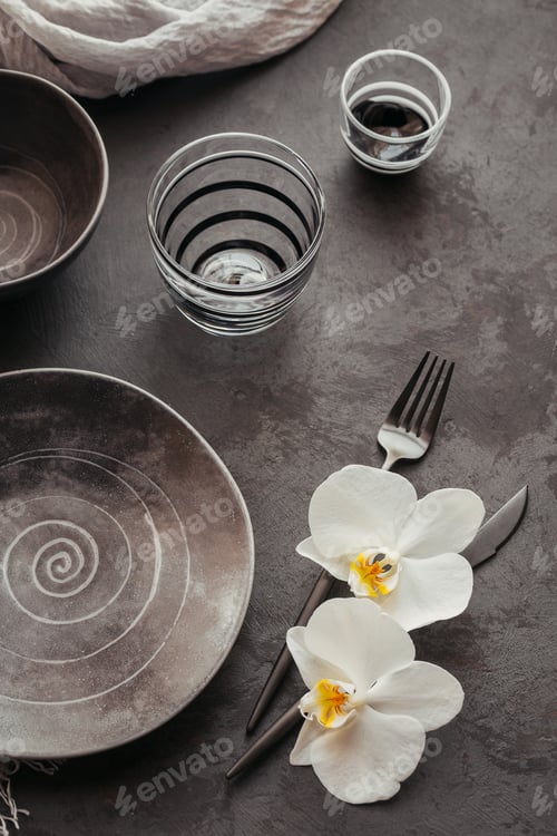 Preview: Elegance table setting with knitted grey napkin, ceramic plates, glasses and white orchid flowers