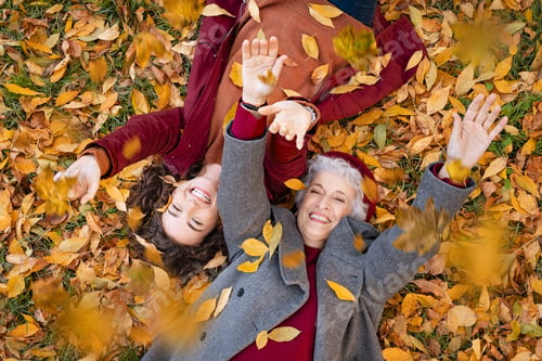 Preview: Grandmother and granddaughter lying on foliage and enjoy the autumn