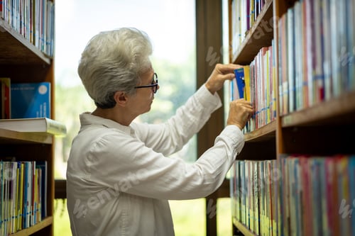 Preview: Elder woman sitting enjoys reading book in quiet of the library