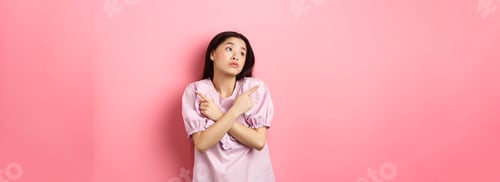 Preview: Indecisive asian woman cant decide, pointing fingers sideways and look pensive aside, making choice