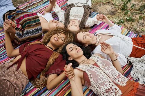 Preview: high angle view of smiling multiethnic women holding hands and lying on blanket in retreat center