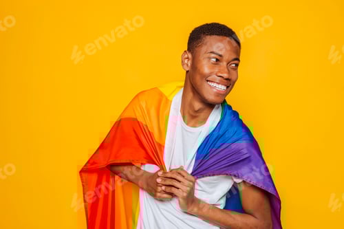 Preview: Happy black man smiling and holding rainbow flag on yellow background