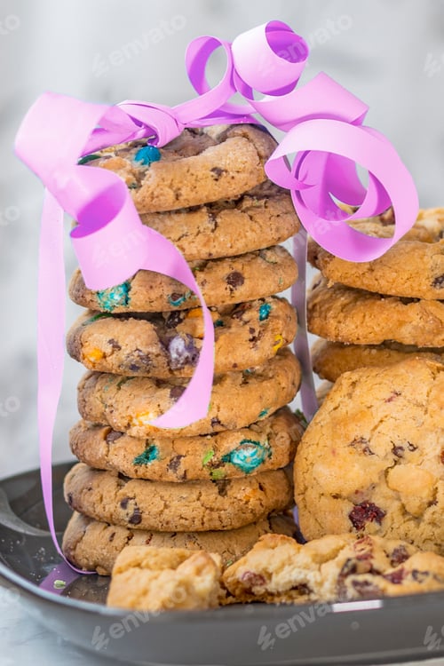 Preview: two stacks of cookies starting with colored chocolate and raisins decorated with pink ribbon