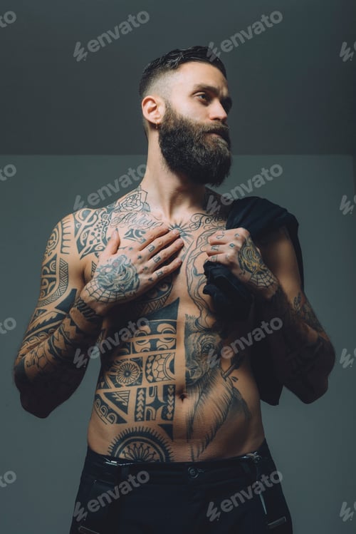 Preview: Portrait of young man with beard, bare chest covered in tattoos