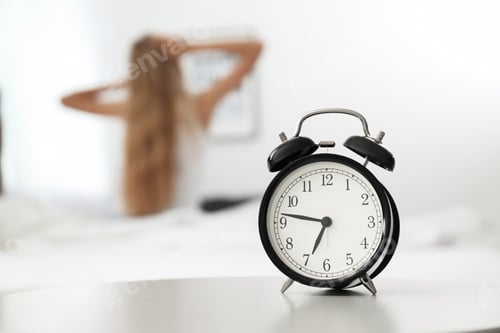 Preview: Analog alarm clock and blurred woman on background. Time of day