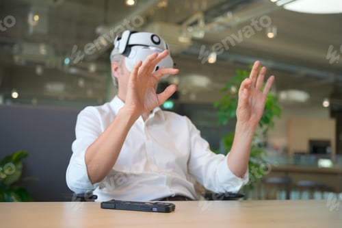 Preview: Man wearing VR headset gesturing with hands in a modern office environment