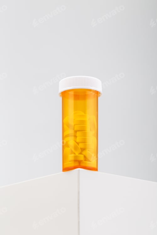 Preview: Vertical shot of a yellow container filled with pills on a white table