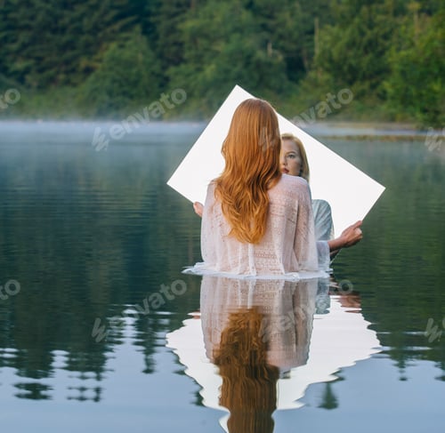 Preview: Rear view of young woman standing in lake holding mirror looking at reflection