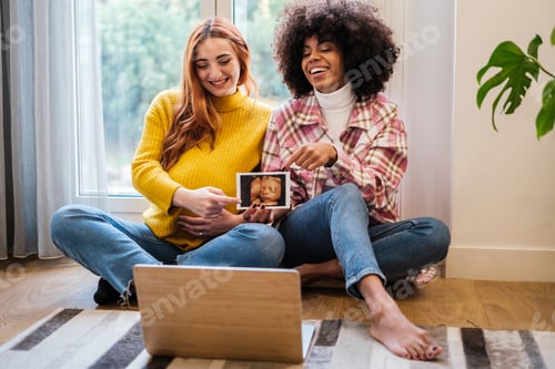 Preview: Lgtbi couple showing the ultrasound of their future child to their family online - motherhood