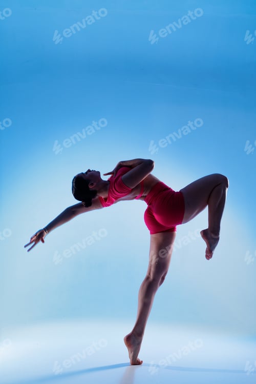 Preview: Vertical photo of woman balancing in dance style backbend pose on blue background with copy space