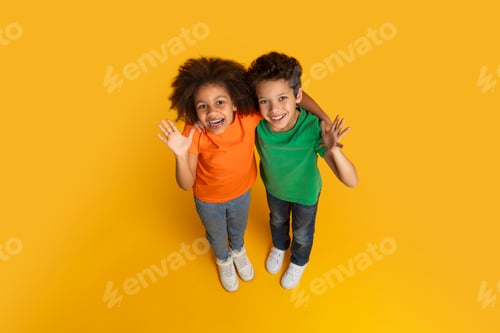 Preview: Enthusiastic kids waving at camera on yellow background