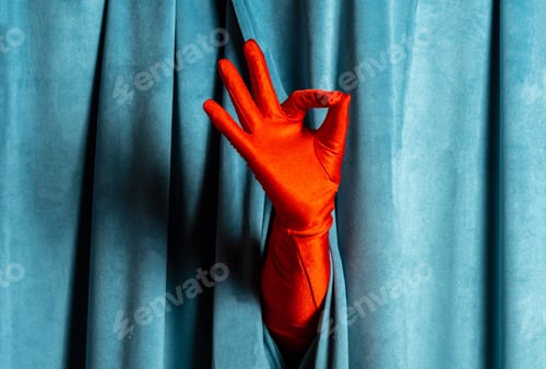 Preview: A woman's hand in a red glove shows an ok sign against a background of blue corduroy curtains