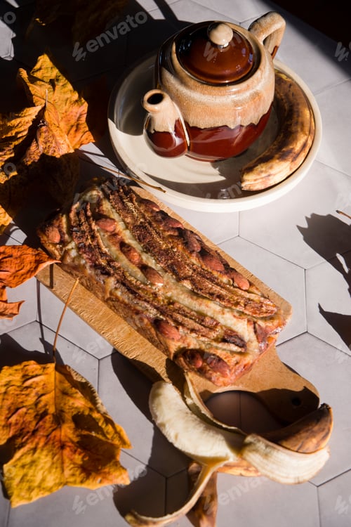 Preview: Still life Banana pie with a ceramic teapot in the rays of the autumn sun on a gray tile table