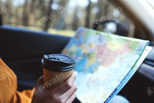 Preview: Closeup image of a woman reading a map for direction and drinking coffee in the car