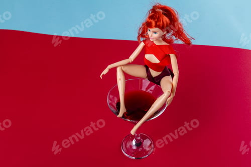 Preview: Ginger female doll sitting on a glass of martini.
