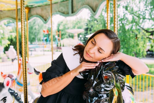 Preview: Woman in dress poses on a bright carousel with horses in summer day. Psychology inner child therapy.