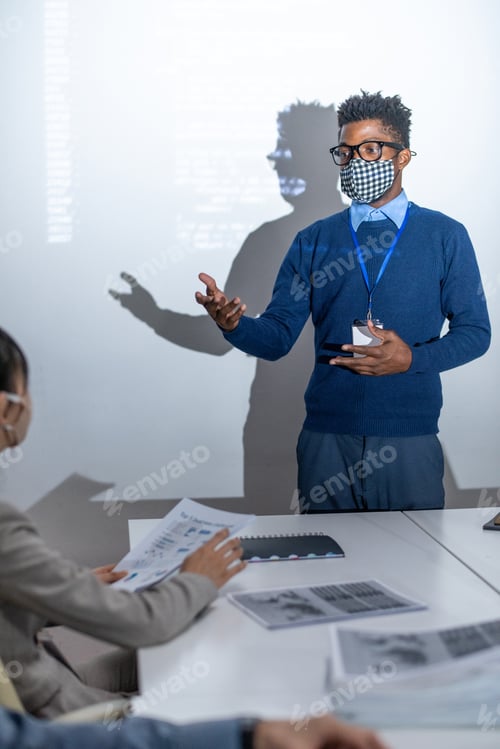 Preview: Young African programmer in protective mask standing by interactive screen