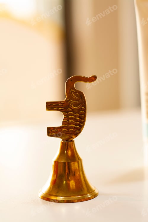 Preview: Vertical shot of a golden elephant bell on the white background with sunlight